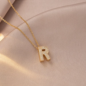 Macro shot of gold R-shaped letter pendant with zircon on soft satin fabric