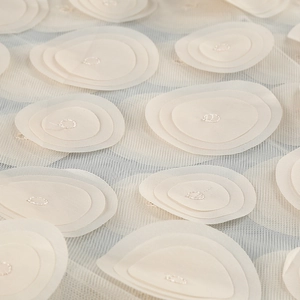 Detailed macro view of white floral lace fabric with polka dot mesh and 3D layered applique