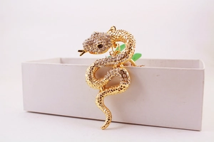 Close-up of golden snake keychain with sparkling rhinestones on a white gift box edge