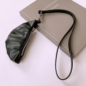 Close-up of minimalist black PU leather croissant pendant with zipper detail on a book