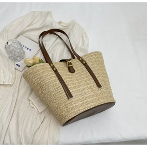 Flat lay of a beige woven straw tote bag with brown leather straps on a white fabric
