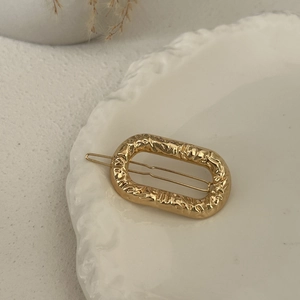 Detail of a golden hammered metal oval hair clip on a white decorative plate with dried flowers