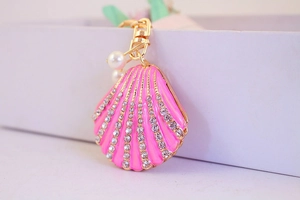 Close-up of pink shell keychain with gold metal frame, clear rhinestones, and pearls