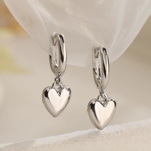 Elegant polished silver heart pendant earrings on a soft beige velvet jewelry display