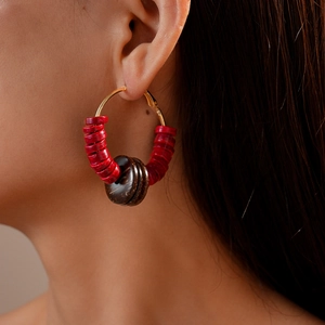 Close-up of geometric coconut shell beaded gold hoop earrings worn on female model