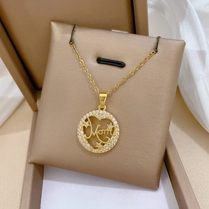 Detail of gold Mom pendant with sparkling stars and pavé crystals on a soft beige display