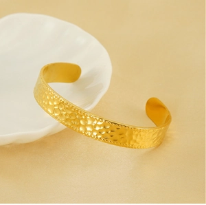 Détail d'un bracelet manchette doré avec texture martelée et bordure perlée élégante