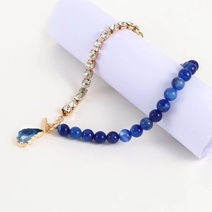 Details der asymmetrischen Goldkette mit weißen Strasssteinen und blauem Steinanhänger