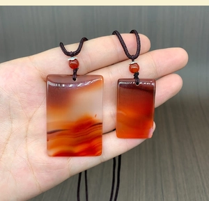 Close-up of translucent red agate pendant set with hand-woven cord on wood background