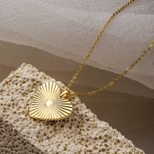 Golden heart pendant necklace with sunburst texture on a minimalist white stone base