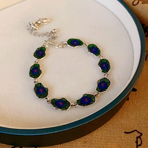 Detail of silver link bracelet with blue and green lotus leaf enamel charms on a tray