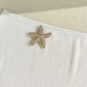 Detailed close-up of a textured gold starfish emblem on white waffle fabric