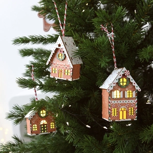 Lighted wooden gingerbread house ornaments hanging on a green Christmas tree