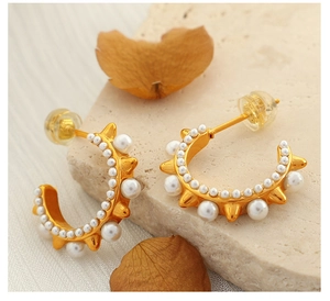 Detailed shot of golden C-shaped hoop earrings with pearls and metallic spikes on stone