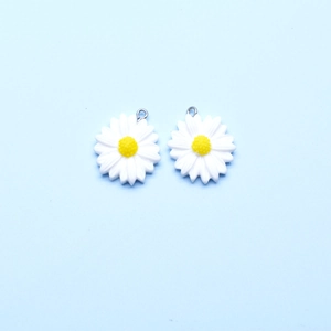 Detailed macro view of two white and yellow resin daisy charms with silver metal loops