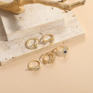 Detail view of five gold evil eye rings with blue zircon set on a beige stone