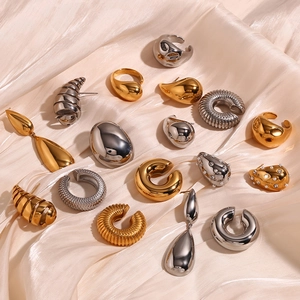 Flat lay of polished teardrop earrings and gold jewelry on pearl satin fabric background