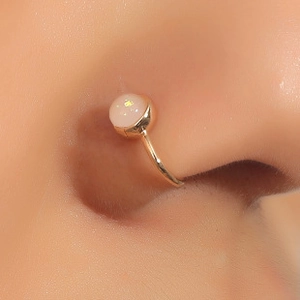 Macro shot of U-shaped non-piercing gold nose clip with a white opal gemstone