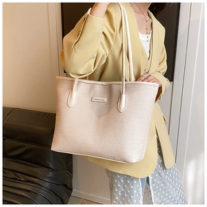 Close-up of beige woven tote bag featuring a leather fashion label and slim shoulder straps
