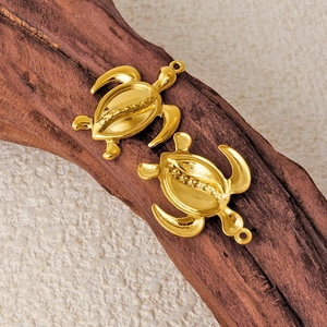 Two golden stainless steel turtle pendants on wood for DIY jewelry making and crafts
