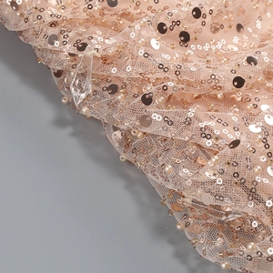 Detail of pink sequin fabric with pearl embroidery and pleated mesh texture on dress