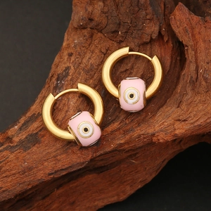 Gold stainless steel hoop earrings with pink evil eye enamel charms on wood background