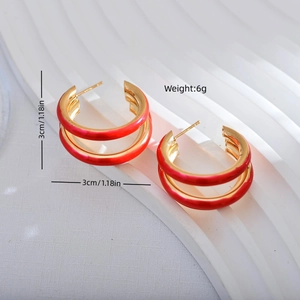 Exaggerated triple-hoop gold-plated red enamel earrings shown on a white textured tray