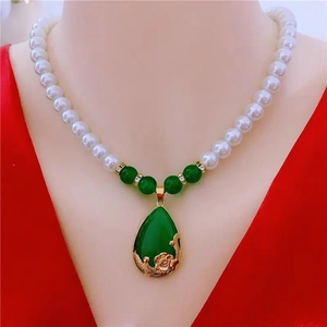 Detail of white pearl necklace with large green teardrop pendant and golden accents