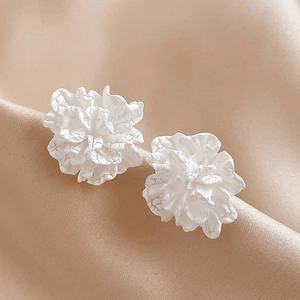 Macro shot of white acrylic flower earrings with 3D texture on soft beige silk