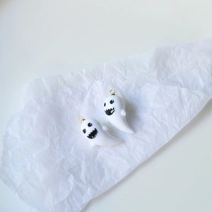 Close-up of white resin ghost charms with black eyes and gold metal hooks for jewelry