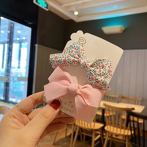 Detail showing two handmade floral fabric bow hair clips on a white display card