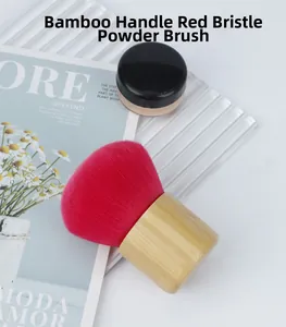 Top view of a soft red mushroom powder brush with a natural bamboo handle on a stylist prop