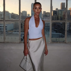 Chic white halter neck top paired with a cream satin midi skirt in a sunset city view