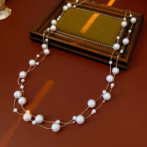 Detailansicht zweilagige Perlenkette mit weißen Perlen und Goldkette auf rotem Grund