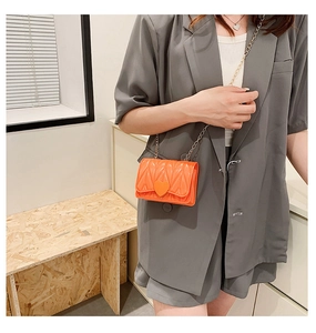 Close-up of orange heart-shaped mini crossbody bag with metal chain on a model