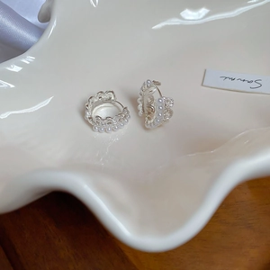 Close-up of elegant crown lace silver hoop earrings with pearls on a ceramic dish