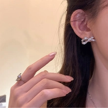 Detailed view of silver bow-shaped earrings and matching ring with zircon inlay