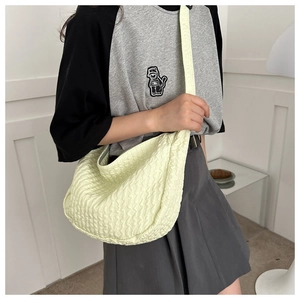 Detail of light yellow textured crossbody bag worn by a model in a minimalist room