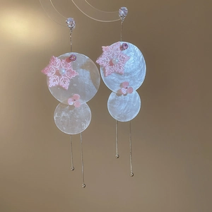 Detail of pearl earrings with shell-shaped plates, floral accents, and silver tassels