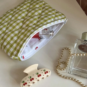 Detail of green gingham makeup bag with cherry print lining and smooth white zipper