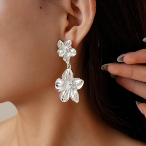 Close-up of model wearing silver flower petal drop earrings with metallic texture