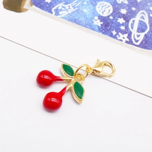 Detail of red cherry pendant with golden lobster clasp and green metal leaves