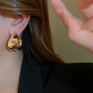 Close-up of model wearing thick gold twisted double-layer hoop earrings in metal style