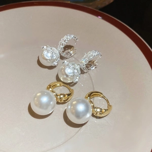 Close-up of gold and silver pearl drop earrings with crystal details on a ceramic dish