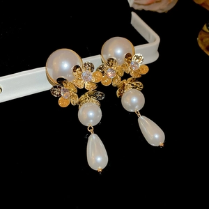Macro detail of gold flower earrings featuring white pearls and sparkling zircon accents