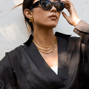 Close-up of a layered gold snake chain necklace and hoop earrings worn by a model