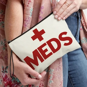 Canvas first aid bag with red MEDS print and wrist strap shown in a hand-held lifestyle shot