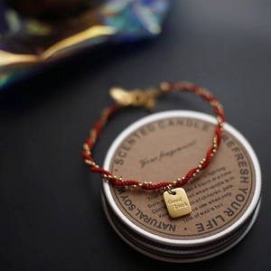 Red string bracelet with gold beads and Good Luck square pendant on display base