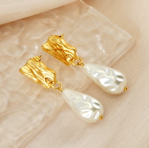 Détail d'une boucle d'oreille dorée en lave avec perle goutte sur fond de soie douce