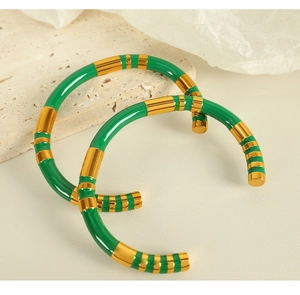 Macro detail of a bright green and gold striped stainless steel open bangle on stone